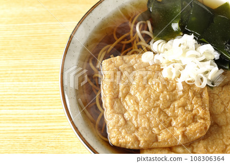 頭頂上的熱騰騰的狐狸蕎麥麵,上面放著兩片炸豆腐、海藻和大蔥。 頭頂上的熱騰騰的狐狸蕎麥麵,上面放著兩片炸豆腐、海藻和大蔥。 108306364