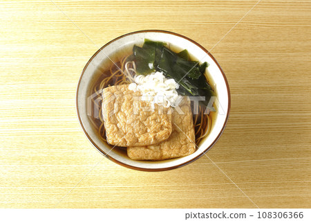 An overhead shot of piping hot fox soba noodles topped with two pieces of fried tofu, seaweed, and green onions. 108306366