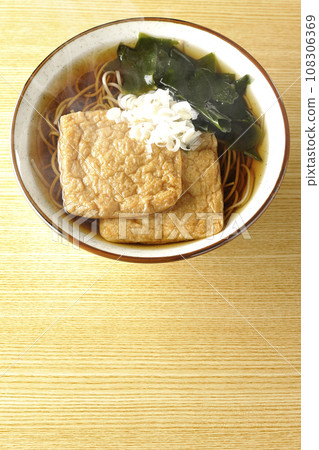 頭頂上的熱騰騰的狐狸蕎麥麵,上面放著兩片炸豆腐、海藻和大蔥。 頭頂上的熱騰騰的狐狸蕎麥麵,上面放著兩片炸豆腐、海藻和大蔥。 108306369