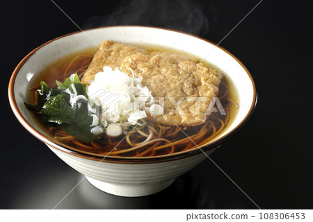 熱狐狸蕎麥麵,上面放著兩片炸豆腐、海藻和大蔥,在黑色背景下拍攝 熱狐狸蕎麥麵,上面放著兩片炸豆腐、海藻和大蔥,在黑色背景下拍攝 108306453