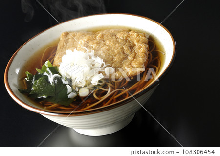 熱狐狸蕎麥麵,上面放著兩片炸豆腐、海藻和大蔥,在黑色背景下拍攝 熱狐狸蕎麥麵,上面放著兩片炸豆腐、海藻和大蔥,在黑色背景下拍攝 108306454