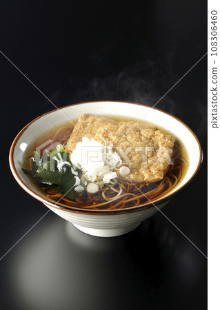 熱狐狸蕎麥麵,上面放著兩片炸豆腐、海藻和大蔥,在黑色背景下拍攝 熱狐狸蕎麥麵,上面放著兩片炸豆腐、海藻和大蔥,在黑色背景下拍攝 108306460