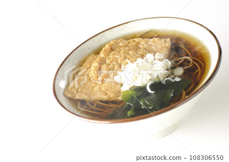 Hot fox soba noodles topped with two pieces of fried tofu, seaweed, and green onions are photographed against a white background. Hot fox soba noodles topped with two pieces of fried tofu, seaweed, and green onions are photographed against a white background. 108306550