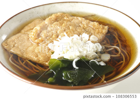在白色背景下拍攝了熱狐狸蕎麥麵,上面放著兩片炸豆腐、海藻和大蔥。 在白色背景下拍攝了熱狐狸蕎麥麵,上面放著兩片炸豆腐、海藻和大蔥。 108306553