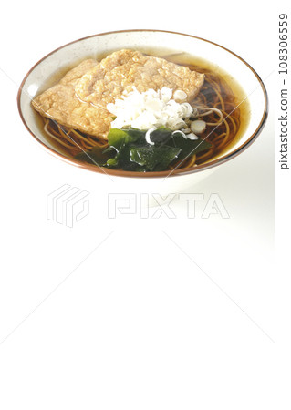 Hot fox soba noodles topped with two pieces of fried tofu, seaweed, and green onions are photographed against a white background. 108306559