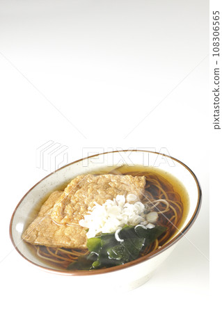 在白色背景下拍攝了熱狐狸蕎麥麵,上面放著兩片炸豆腐、海藻和大蔥。 在白色背景下拍攝了熱狐狸蕎麥麵,上面放著兩片炸豆腐、海藻和大蔥。 108306565