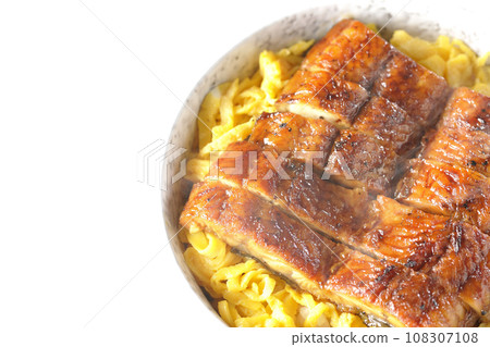 An overhead shot of a piping hot rice bowl of kinshi omelet and kabayaki eel against a white background 108307108