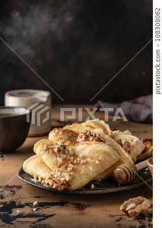 Crepes or thin pancakes with honey and nuts on brown plate over wooden background. Delicious homemade crepes for breakfast dark moody, copy space 108308062