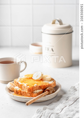 Toasts with butter, banana slices and honey on light kitchen background. Homemade breakfast sandwich. Healthy vegan food concept 108308091