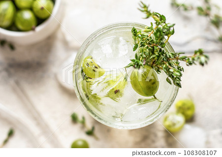 Glass of refreshing iced detox drink with gooseberries and thyme. Infused water or berry cocktail close up top view Glass of refreshing iced detox drink with gooseberries and thyme. Infused water or berry cocktail close up top view 108308107