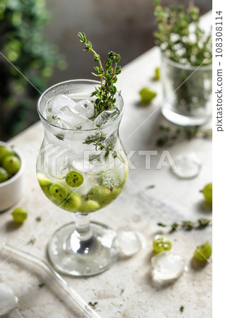 Glass of refreshing iced detox drink with gooseberries and thyme. Infused water or berry cocktail 108308114