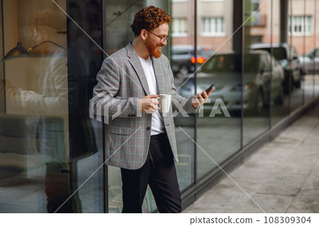 Handsome male freelancer holding phone while standing near office during break time Handsome male freelancer holding phone while standing near office during break time 108309304