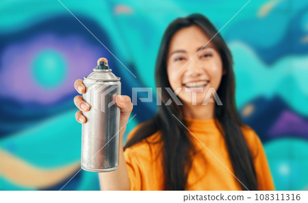 Smiling female street artist pointing spray paint can to camera 108311316