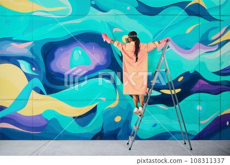 Female street artist painting colorful graffiti standing on a ladder Female street artist painting colorful graffiti standing on a ladder 108311337