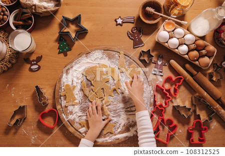 Making gingerbread at home. Little girl cutting cookies of gingerbread dough. Christmas and New Year traditions concept. Christmas bakery. Happy holidays. Top view 108312525