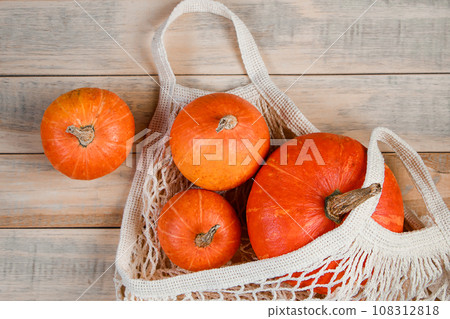 Ripe pumpkins in mesh bag on wooden background. Eco-friendly farm products. Autumn harvest and Thanksgiving concept. 108312818