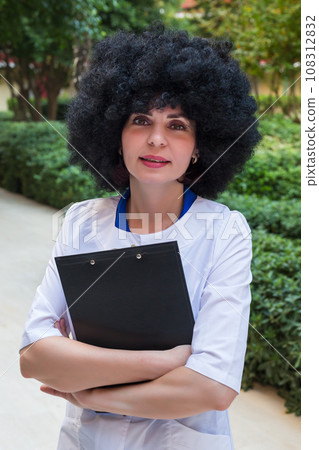Girl medic with black curly hair with a folder of documents outdoors Girl medic with black curly hair with a folder of documents outdoors 108312832