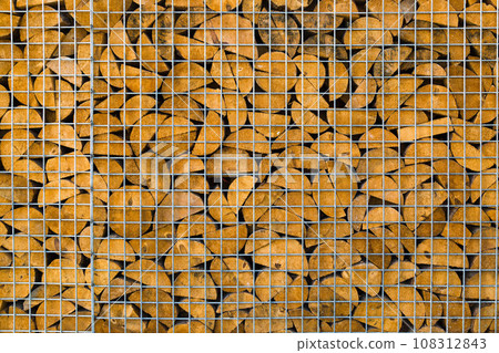 Wooden firewood logs are stacked behind a metal mesh. Wood texture and metal lattice 108312843