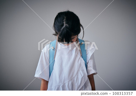 Elementary school girl holding a school bag and looking down Elementary school girl holding a school bag and looking down 108313357
