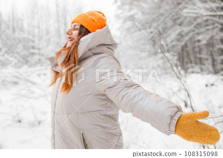 Happy young adult caucasian woman in a hat breathing fresh air in the winter forest. Winter vacations concept 108315098