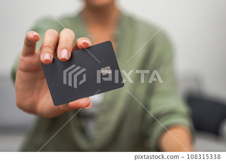 A close-up reveals a lady's hand displaying a dark credit card with a chip, ideal for contactless payments, illustrating online shopping and mobile banking. A close-up reveals a lady's hand displaying a dark credit card with a chip, ideal for contactless payments, illustrating online shopping and mobile banking. 108315338