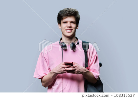 Young male with headphones holding smartphone, on grey background 108315527