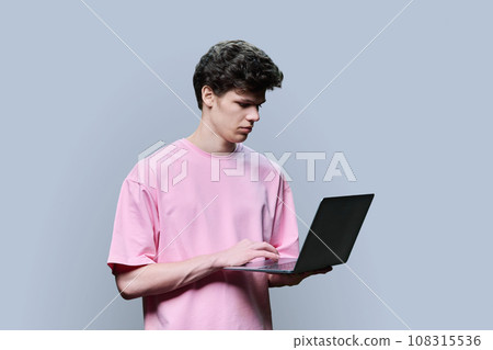 Young male college student using laptop, grey studio background Young male college student using laptop, grey studio background 108315536