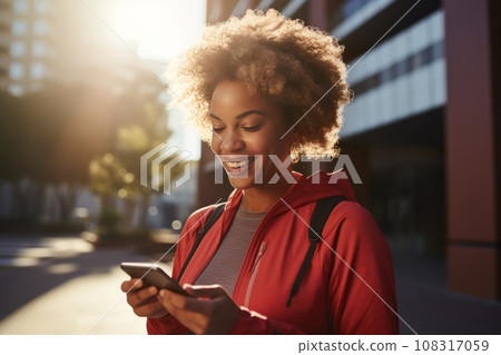 Athletic young African American woman in sports outfit with smartphone while training outdoor. Slender black lady resting after jogging or walking in city street. Active lifestyle in urban environment Athletic young African American woman in sports outfit with smartphone while training outdoor. Slender black lady resting after jogging or walking in city street. Active lifestyle in urban environment 108317059