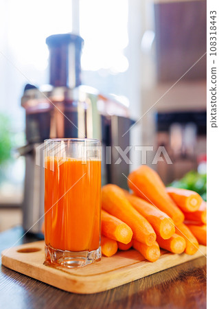 Glass of freshly squeezed carrot juice, carrots and juicer in the kitchen Glass of freshly squeezed carrot juice, carrots and juicer in the kitchen 108318443