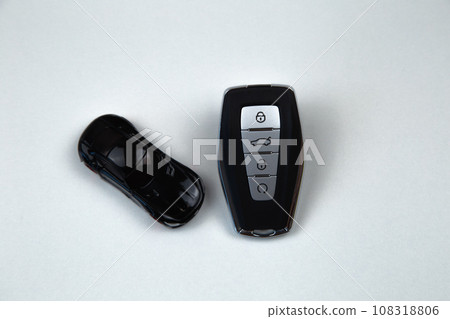 The car keys are black with metal inserts and automatic opening and closing buttons lying on a white background, next to a black car. High quality photo The car keys are black with metal inserts and automatic opening and closing buttons lying on a white background, next to a black car. High quality photo 108318806