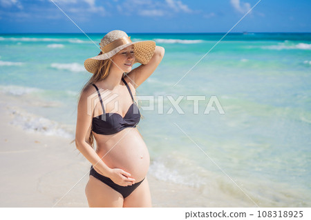 Radiant and expecting, a pregnant woman stands on a pristine snow-white tropical beach, celebrating the miracle of life against a backdrop of natural beauty 108318925