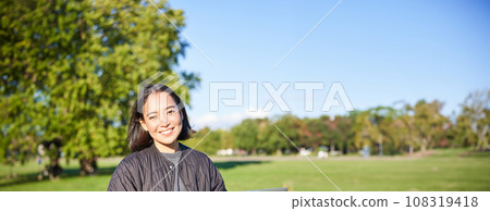 Young asian woman working remotely, freelance girl sits in park with laptop, doing her job from outdoors Young asian woman working remotely, freelance girl sits in park with laptop, doing her job from outdoors 108319418