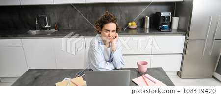 Image of young working woman, looking at laptop, sitting at home and watching webinar, connecting to team meeting, studying indoors Image of young working woman, looking at laptop, sitting at home and watching webinar, connecting to team meeting, studying indoors 108319420