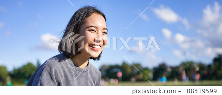 Vertical shot of happy korean girl sitting in park, learning how to play ukulele, singing and relaxing 108319599