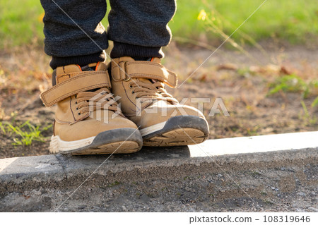 Feet of a little boy in brown nubuck shoes in autumn in a city park. Comfortable waterproof demi-season shoes Feet of a little boy in brown nubuck shoes in autumn in a city park. Comfortable waterproof demi-season shoes 108319646