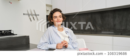 Portrait of young woman at home, working, writing in notebook, taking notes or doing homework Portrait of young woman at home, working, writing in notebook, taking notes or doing homework 108319686