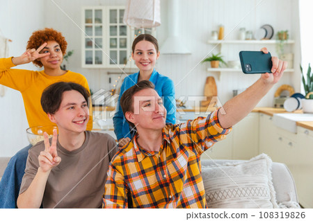 Cheers Funky mood. Happy group of friends make selfie. Man taking photo of friends at party. Group of multiracial young people taking photo on phone. Young people enjoy their company smile have fun 108319826
