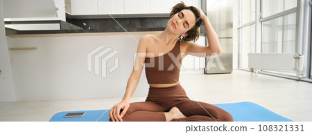 Image of yoga girl in sportswear, stretches her neck, workout, training at home in bright room Image of yoga girl in sportswear, stretches her neck, workout, training at home in bright room 108321331