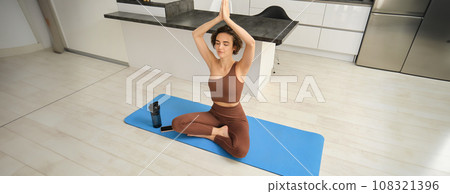 Portrait of fit and healthy woman in sportswear, doing yoga at home on fitness mat, making asana, relaxing and meditating indoors Portrait of fit and healthy woman in sportswear, doing yoga at home on fitness mat, making asana, relaxing and meditating indoors 108321396
