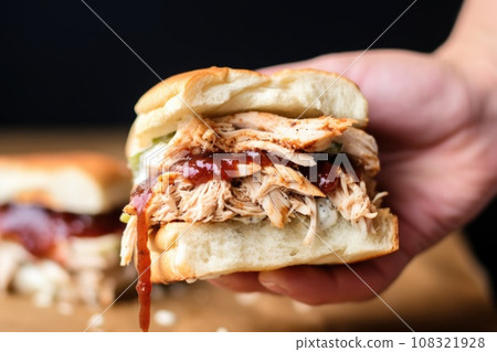 hand holding sandwich filled with alabama chicken and white bbq sauce 108321928