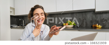 Portrait of beautiful woman at home, holding smartphone, online shopping from mobile phone app 108321939