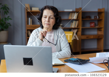 Confident stylish european middle aged senior woman using laptop at home. Stylish older mature 60s lady sitting at table looking at computer screen typing chatting reading writing email Confident stylish european middle aged senior woman using laptop at home. Stylish older mature 60s lady sitting at table looking at computer screen typing chatting reading writing email 108323129