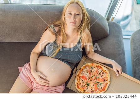 A pregnant woman enjoys a slice of pizza, savoring a moment of indulgence while satisfying her craving for a delightful, comforting treat. Excited Pregnant Young Lady Enjoying Pizza Holding Biting 108323444
