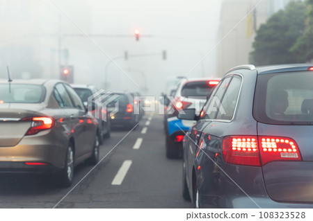Scenic city road traffic light jam wim many cars at foggy misty rainy haze morning low poor visibility cold spring autumn season. Seasonal bad rainy weather accident danger warning car fog light 108323528