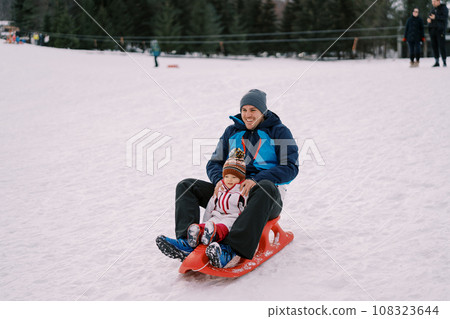 Laughing dad with a little girl sledding down a hill 108323644