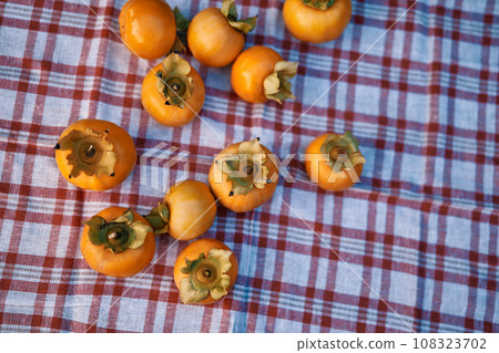 Ripe persimmons lie on a checkered napkin on the table Ripe persimmons lie on a checkered napkin on the table 108323702