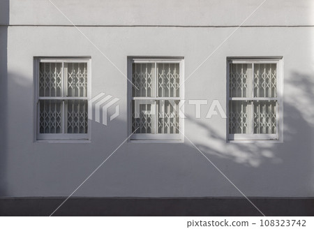 House exterior with triple wooden casement windows on white wall and white steel folding gates inside. 108323742