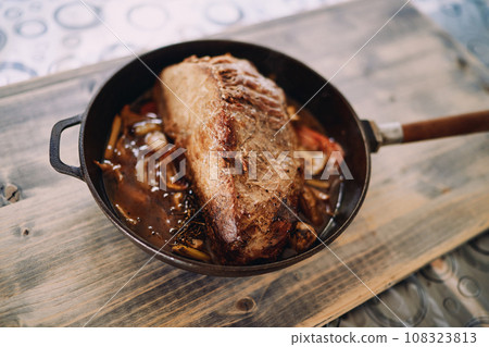 Frying pan with roast beef with vegetables stands on a wooden table Frying pan with roast beef with vegetables stands on a wooden table 108323813