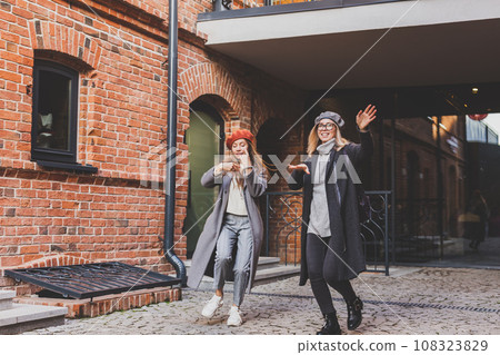 Millennial young women having fun and dance on city street. Female funny friends enjoying autumn day around the city. 108323829
