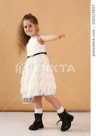 little model girl with long brown hair in designer white dress with belt, military boots full body photo walking. little model girl with long brown hair in designer white dress with belt, military boots full body photo walking. 108324607